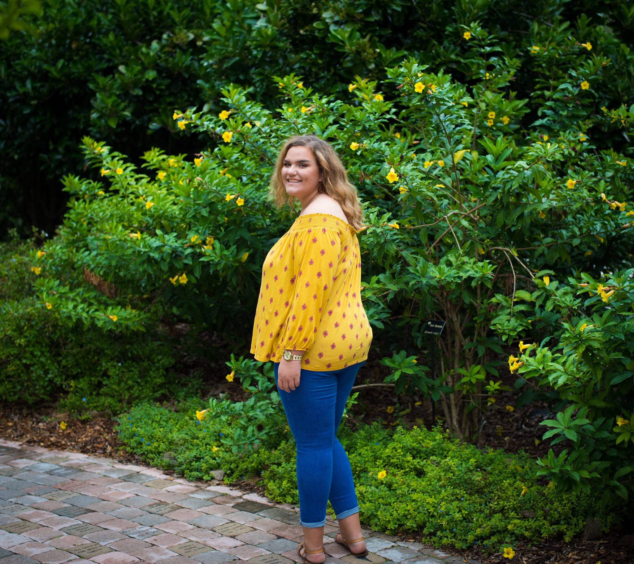 Senior portrait at botanical garden with yellow flowering shrubs in Tampa Bay